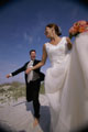 Casal recém-casado a correr na areia. O noivo de fato e a noiva de vestido de noiva com boutet
